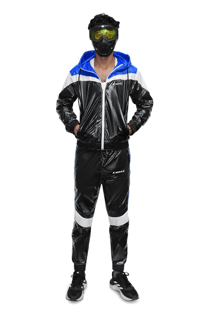 A person modeling a shiny black, white, and blue hooded tracksuit with a glossy vinyl-like finish, standing against a plain white background. The tracksuit has a blue hood lining, white shoulder panels, and white side stripes on the pants.